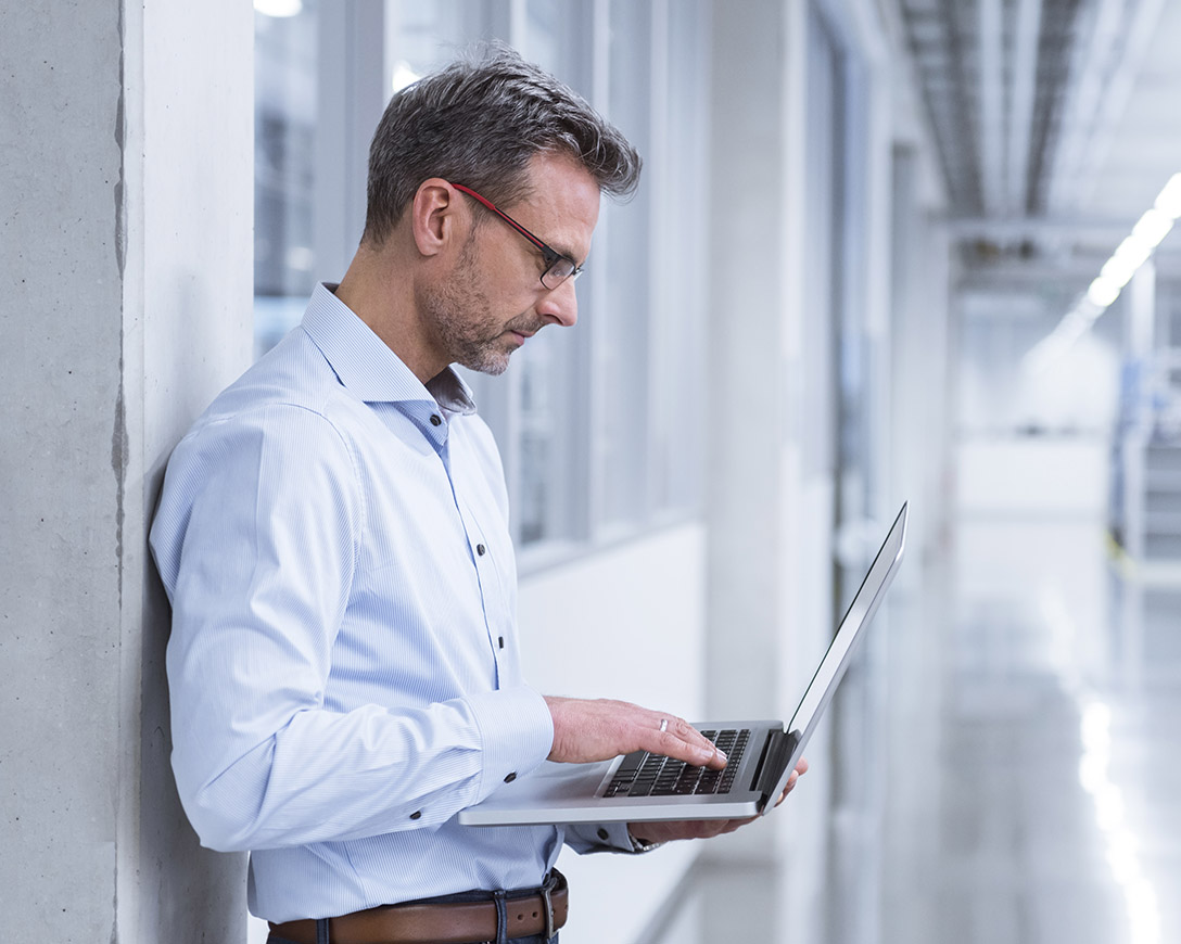 Next Generation – A man leans against a concrete wall and works on his laptop