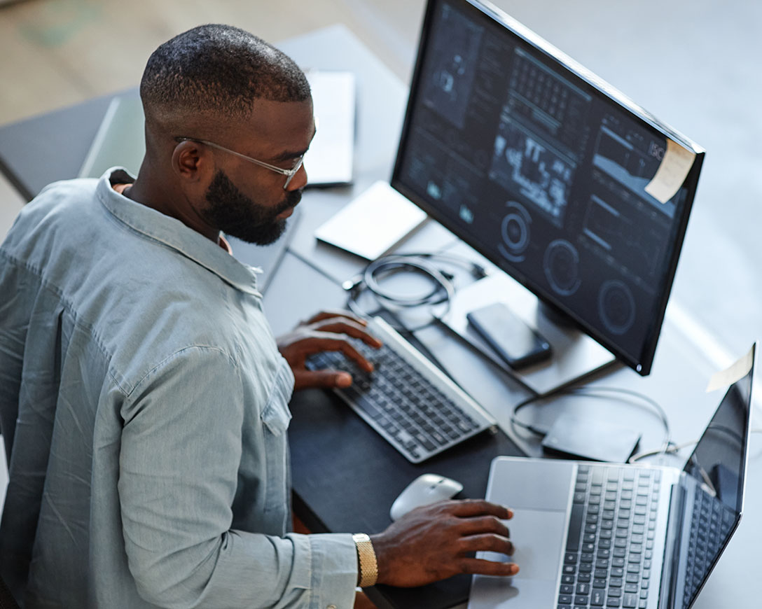 Security – A man works simultaneously on a laptop and a desktop computer