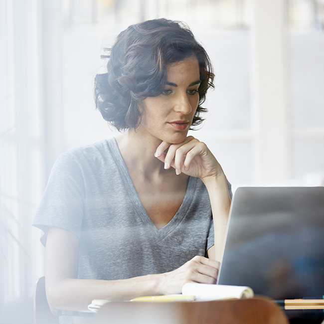 A woman in a bright environment sits focused on her laptop