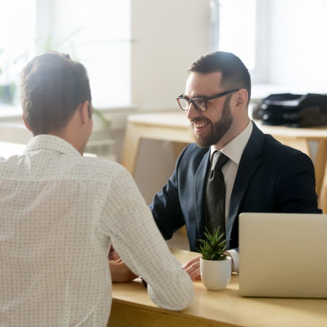 Two individuals dressed in formal attire engaged in a conversation while seated at a desk