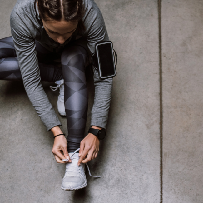 Une femme laçant ses chaussures sur un sol en béton, se préparant à ses activités quotidiennes avec concentration et détermination.