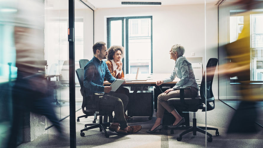 Réunion d'affaires avec trois personnes à une table de conférence dans un bureau.