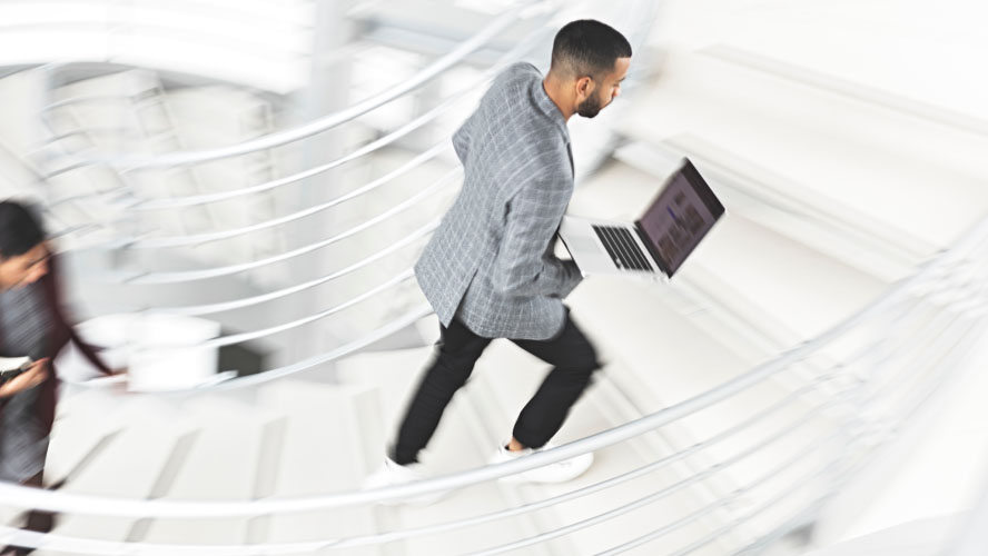 A businessman confidently descends stairs with a laptop in hand, embodying professionalism and productivity.