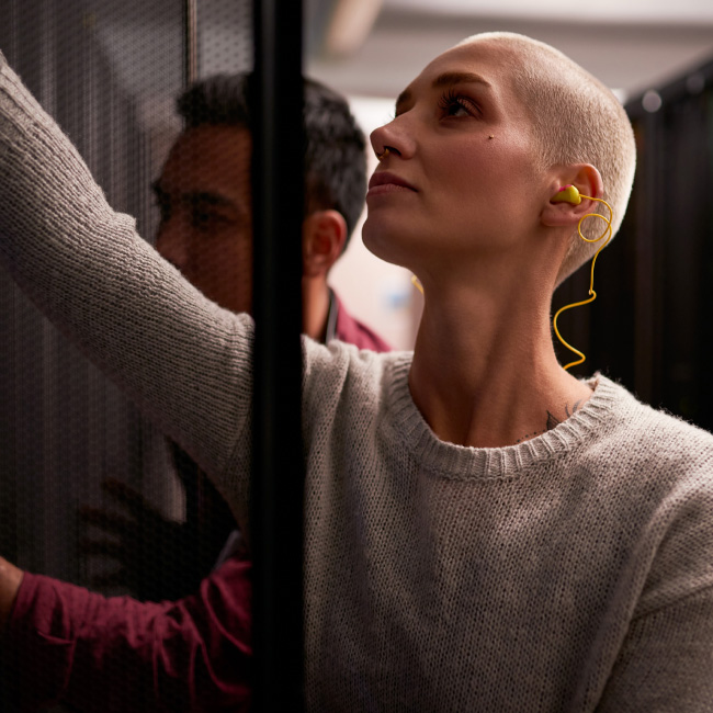 A woman sporting a shaved head and a yellow earbud.