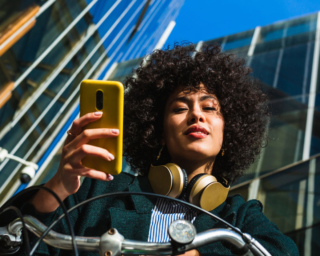 Une femme aux cheveux bouclés portant des écouteurs tout en utilisant son téléphone pour écouter de la musique.