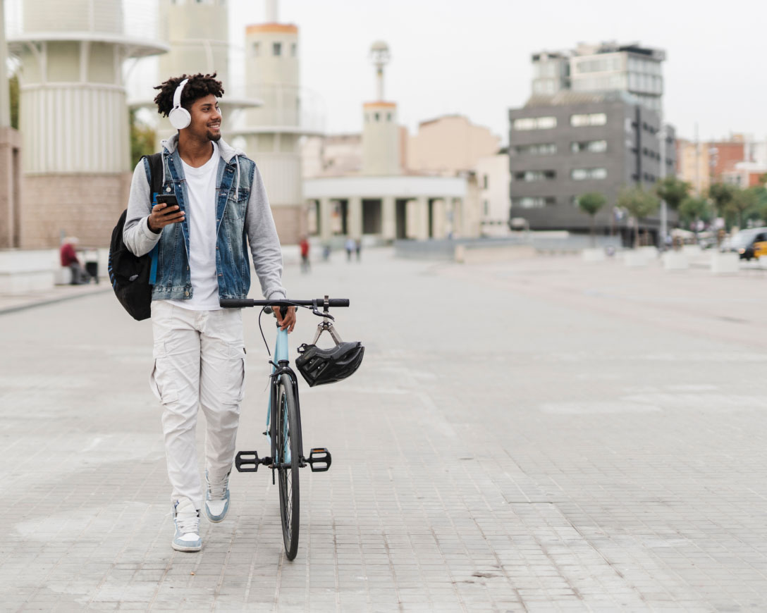 Un cycliste portant des écouteurs se promène dans la rue, appréciant la musique tout en marchant avec son vélo.