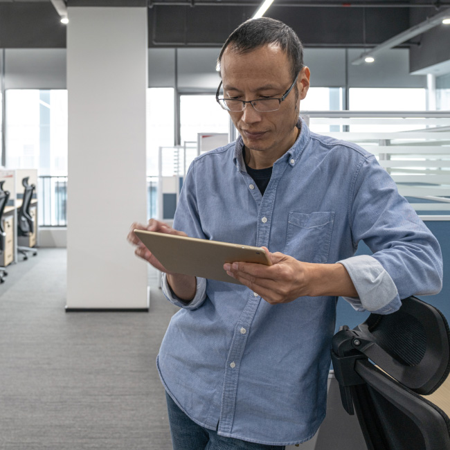 A man in a blue shirt using a tablet device, engrossed in its screen, displaying focused and attentive interaction.